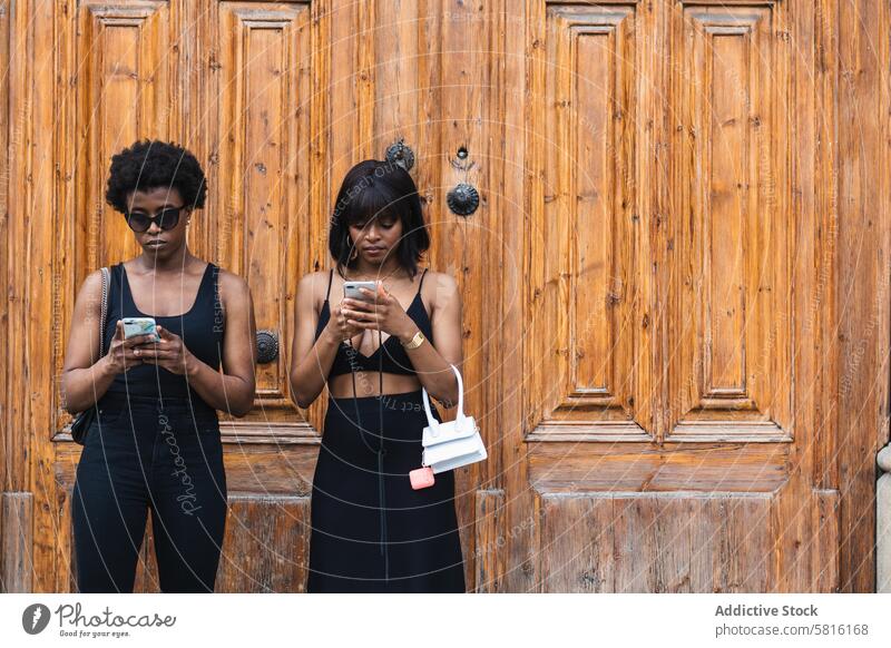 Schwarze Frauen benutzen Smartphones, während sie auf der Straße stehen Surfen benutzend Zusammensein soziale Netzwerke digital Sucht Internet online Browsen