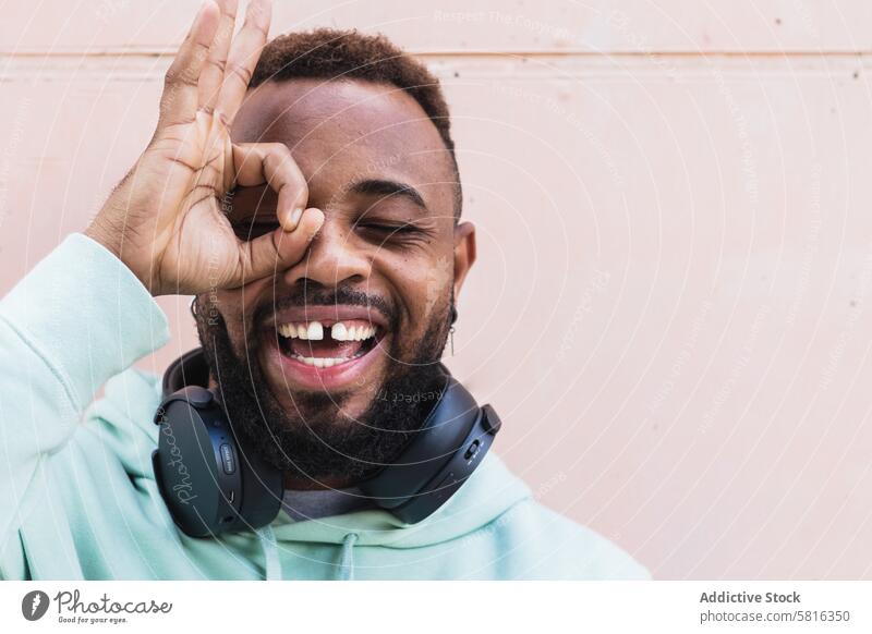 Erfreuter ethnischer Hipster-Mann mit okayer Geste heiter Finger gestikulieren Glück Kopfhörer Vollbart lässig Erwachsener Afroamerikaner schwarz Spaß haben