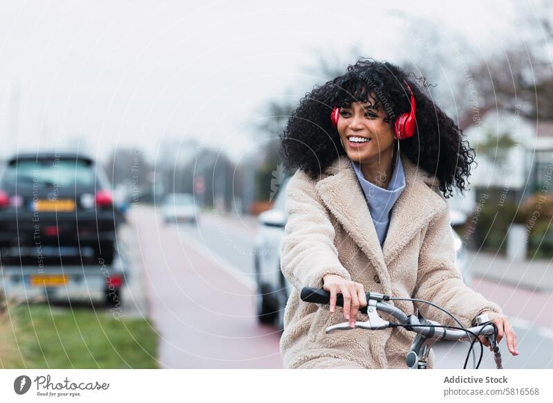 Aufgeregte schwarze Frau mit Kopfhörern beim Fahrradfahren benutzend Musik zuhören Straße PKW Mitfahrgelegenheit Kälte Großstadt Porträt afroamerikanische Frau