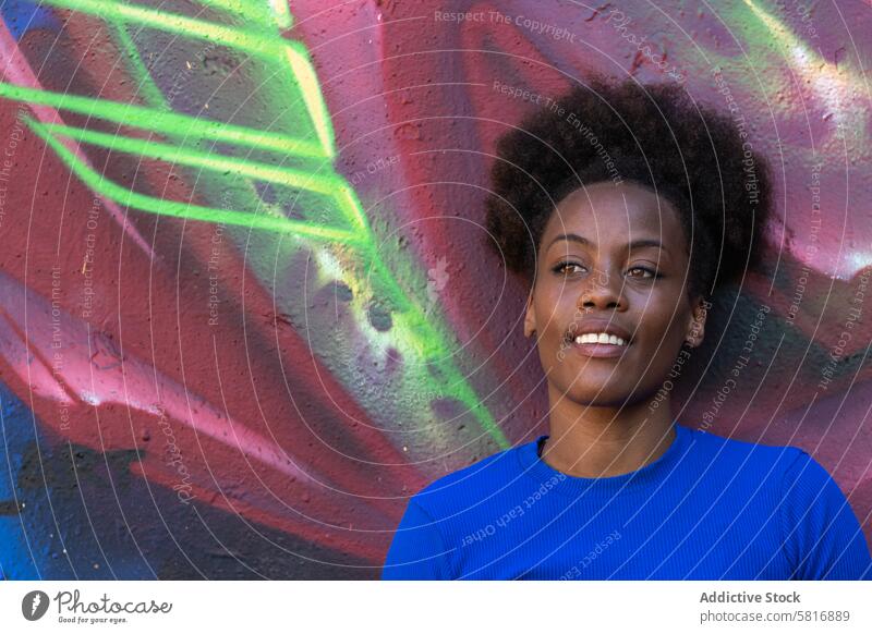 Schwarze Frau steht an einer Wand mit Graffiti Großstadt fettarm sich[Akk] entspannen urban cool Straßenkunst Lächeln ethnisch schwarz Afroamerikaner farbenfroh
