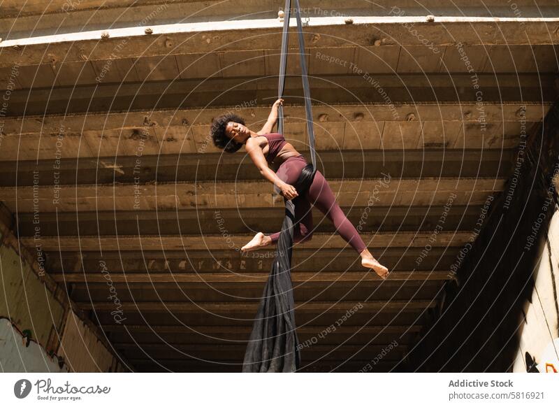 Schlanke Frau macht Yoga mit Aerial Silks in der Stadt Hängematte Antenne Seide Gurt Gleichgewicht üben Pose akrobatisch schlanke Großstadt ethnisch