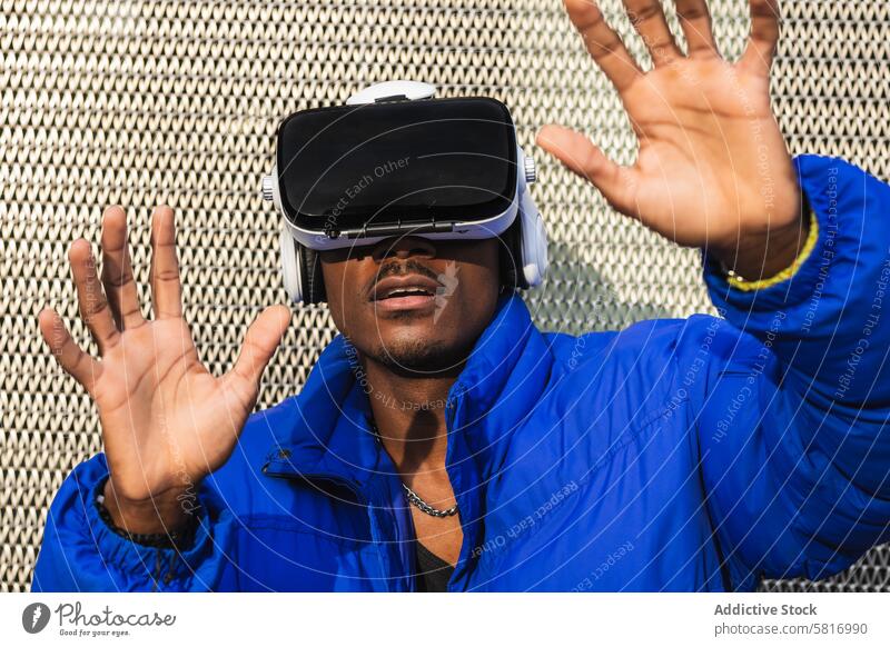 Schwarzer Mann erlebt die virtuelle Realität in der Stadt Virtuelle Realität Schutzbrille VR Brille Erfahrung interagieren berühren futuristisch Großstadt