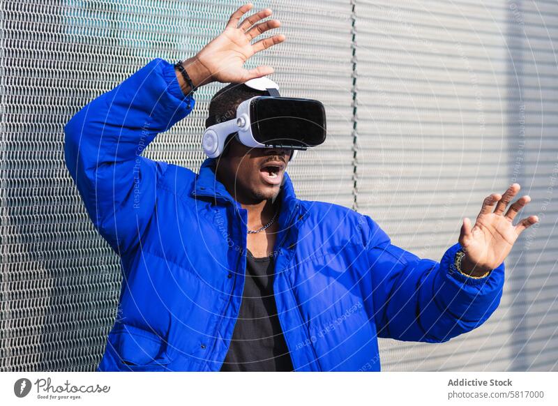 Schwarzer Mann erlebt die virtuelle Realität in der Stadt Virtuelle Realität Schutzbrille VR Brille Erfahrung interagieren berühren futuristisch Großstadt