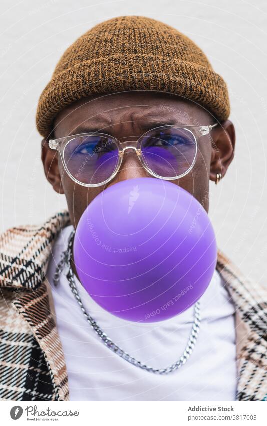 Trendy ethnischen Mann bläst Ballon Schlag Luftballon Stil urban Straße lässig jung Großstadt modern männlich schwarz Afroamerikaner Hut Brille Mode Outfit