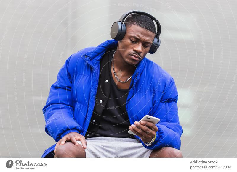 Schwarzer Mann mit Kopfhörer auf Smartphone in der Stadt zuhören Musik Windstille Gesang Drahtlos Großstadt Straße männlich ethnisch schwarz Afroamerikaner