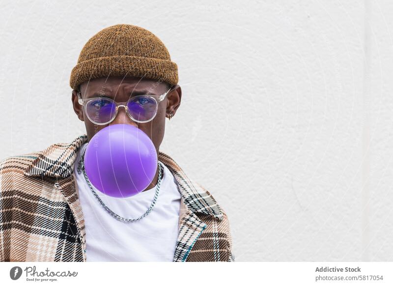 Trendy ethnischen Mann bläst Ballon Schlag Luftballon Stil urban Straße lässig jung Großstadt modern männlich schwarz Afroamerikaner Hut Brille Mode Outfit