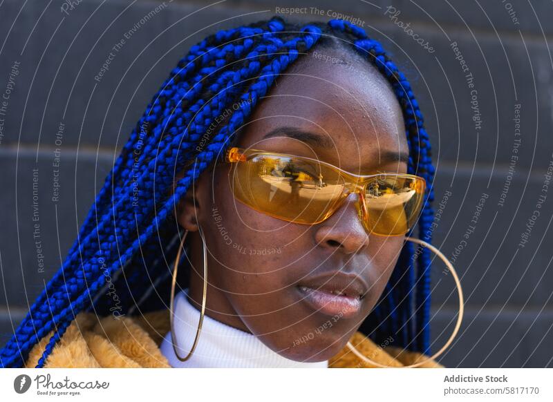 Stilvolle schwarze Frau in gelbem Mantel in der Stadt lebhaft Outfit blaue Haare ausgefallen trendy Geflecht ethnisch Afroamerikaner Frisur Mode Großstadt