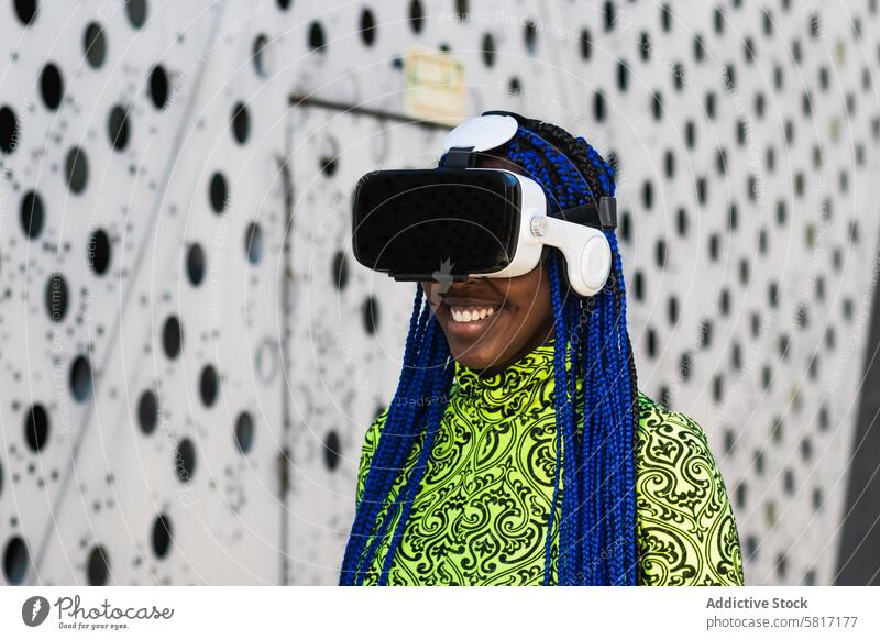 Schwarze Frau im VR-Headset in der Stadt Virtuelle Realität interagieren Erfahrung Schutzbrille Straße ethnisch schwarz Afroamerikaner blaue Haare Geflecht