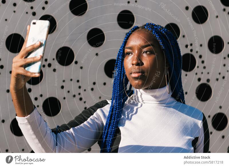 Ernste schwarze Frau nimmt Selfie auf der Straße blaue Haare Geflecht Frisur Behaarung ernst trendy Farbe Smartphone ethnisch Afroamerikaner Umwelt Foto urban