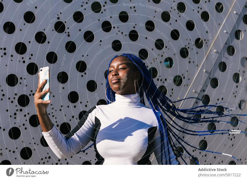 Ernste schwarze Frau nimmt Selfie auf der Straße blaue Haare Geflecht Frisur Behaarung ernst trendy Farbe Smartphone ethnisch Afroamerikaner Umwelt Foto urban