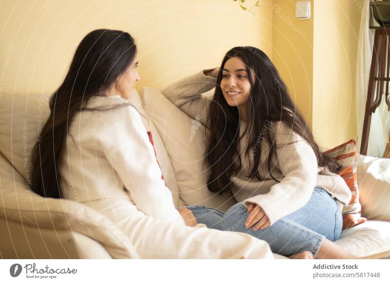 Lächelnde junge Frau im Gespräch mit ihrer Mutter auf einem Sofa zu Hause sitzen. Erwachsener Liebe Tochter heimwärts sprechend Lifestyle Familie Menschen
