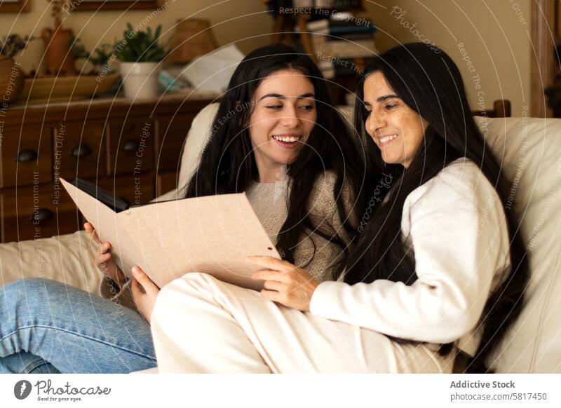 Reife Mutter und erwachsene Tochter lächelnd, während sie ein Fotoalbum betrachten heimwärts Frau Zusammensein Album jung Kind Glück Menschen Eltern Haus Buch
