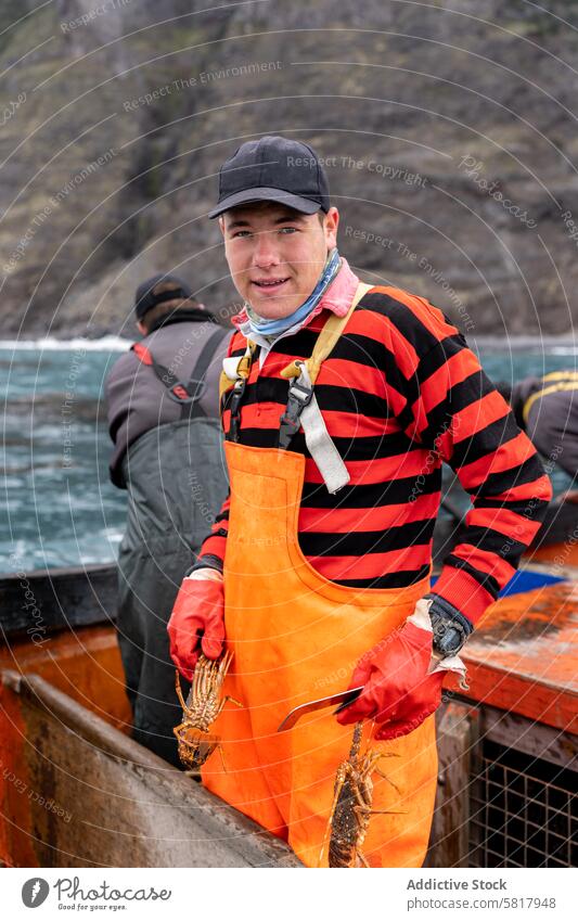 Porträt eines jungen Fischers in Schürze bei der Arbeit mit Hummern vertikal Mann Kaukasier Lächeln in die Kamera schauen stehen Handschuhe arbeiten Beteiligung
