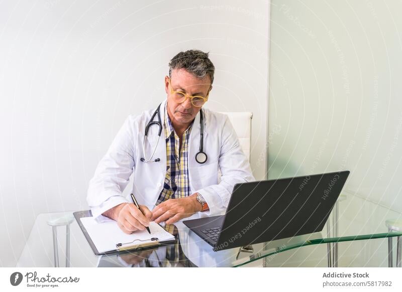 Männlicher Arzt arbeitet mit Laptop und Klemmbrett in einer Arztpraxis Analysieren Gesundheitswesen und Medizin Beruf Berufliche Tätigkeit kardial Pflege prüfen