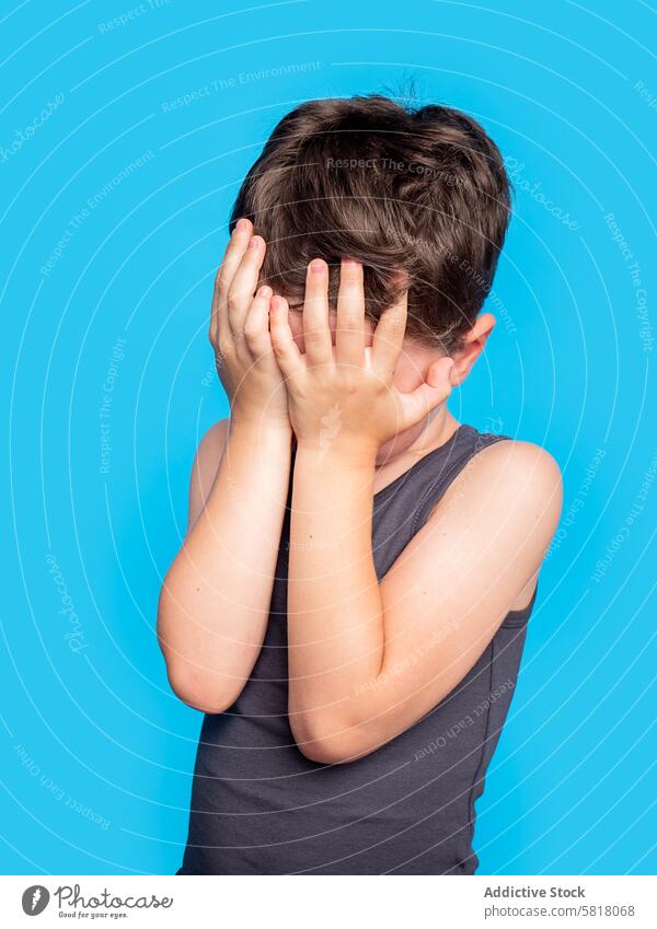 Junger Junge versteckt Gesicht mit Händen auf blauem Hintergrund Kind versteckend Studioaufnahme jung Wegsehen verzweifelt verärgert Spielen Emotion Ausdruck