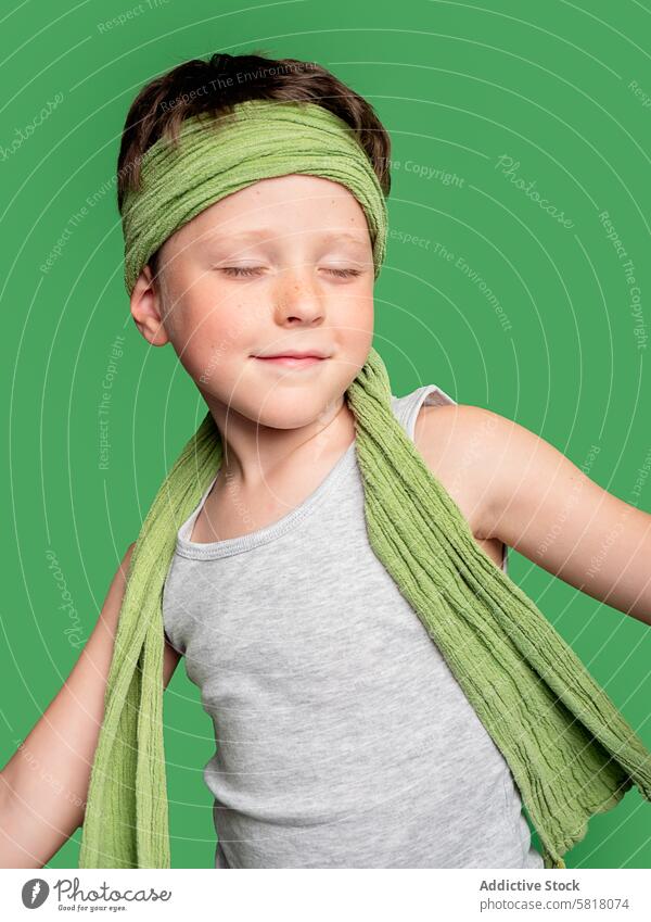 Junge mit geschlossenen Augen und grünem Kopftuch, Studioaufnahme Kind grüner Hintergrund Tanktop grau Augen geschlossen Inhalt jung Lächeln entspannt Mode Stil