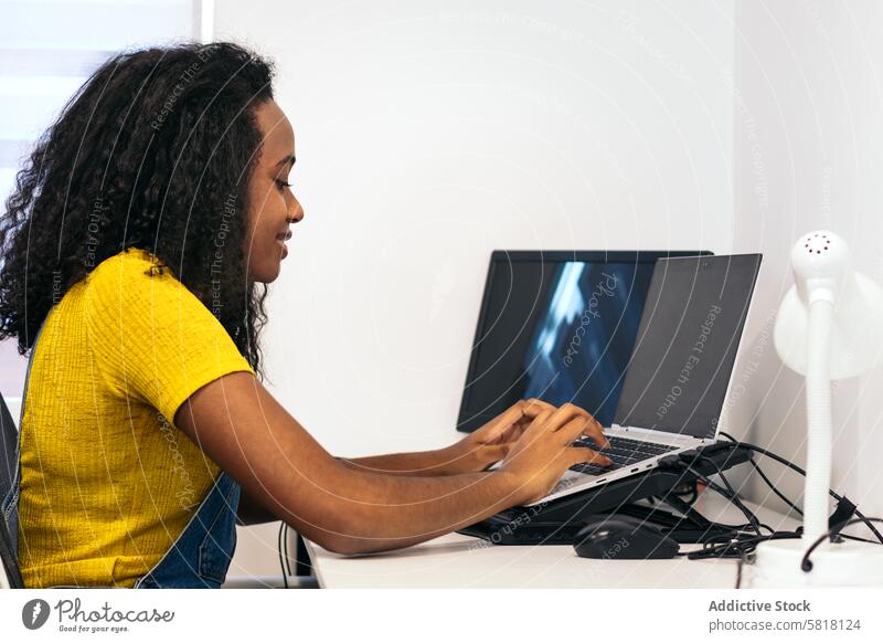 Junge schwarze Frau, die aus der Ferne mit einem Laptop arbeitet Junge Frau Heimarbeitsplatz Arbeit Fernarbeit Afroamerikaner Produktivität digitaler Nomade