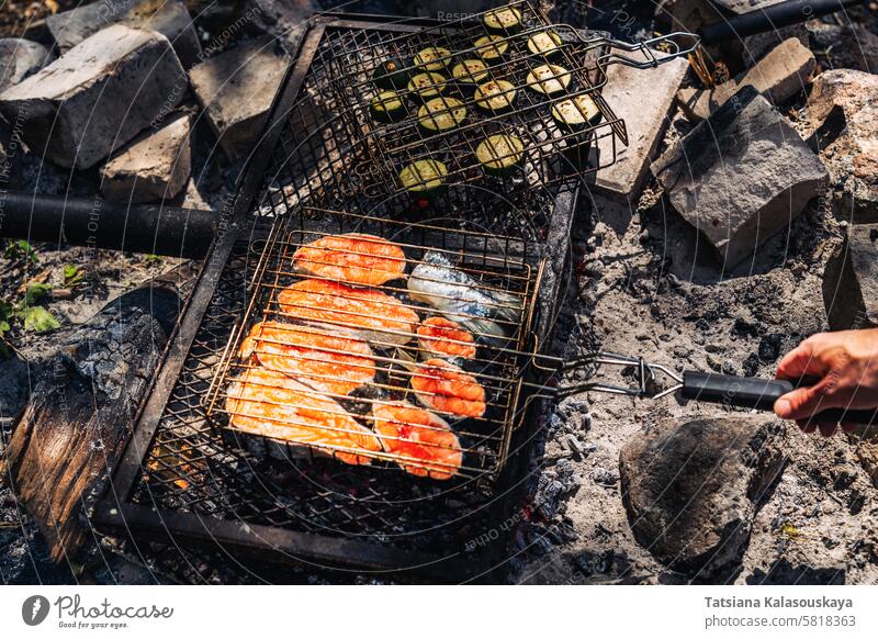 Lachssteaks und Zucchinibecher, gegrillt auf einem Grill über einem Lagerfeuer bei einem Picknick im Wald Steaks Tassen Grillrost Wälder Fisch Essen zubereiten