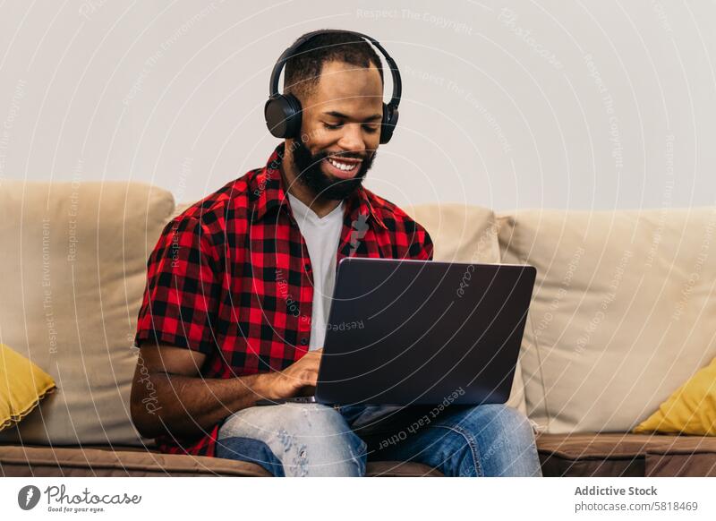 Afroamerikanischer Mann, der von zu Hause aus mit seinem Laptop arbeitet Telearbeit Computer Afroamerikaner heimwärts Internet freiberuflich abgelegen online