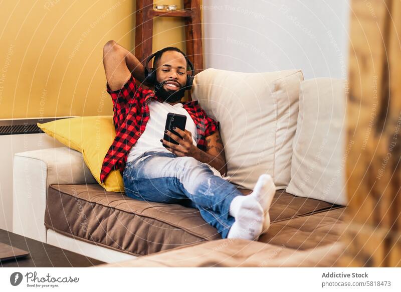 Afroamerikanischer Mann entspannt sich mit seinem Smartphone auf dem Sofa zu Hause heimwärts schwarz Liege Afroamerikaner Mobile Technik & Technologie Telefon