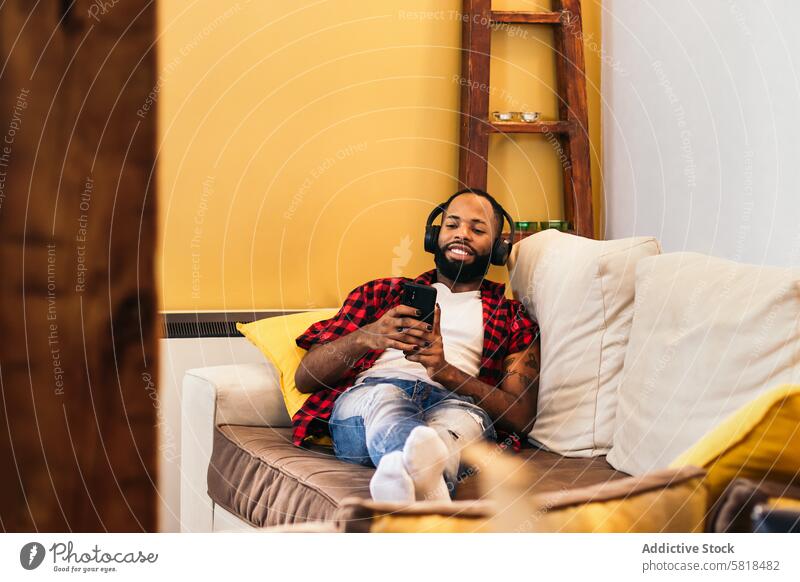 Afroamerikanischer Mann entspannt sich mit seinem Smartphone auf dem Sofa zu Hause heimwärts schwarz Liege Afroamerikaner Mobile Technik & Technologie Telefon
