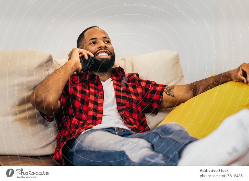 Ein afroamerikanischer Mann telefoniert entspannt zu Hause mit seinem Smartphone Sofa heimwärts schwarz Liege Afroamerikaner Mobile Technik & Technologie