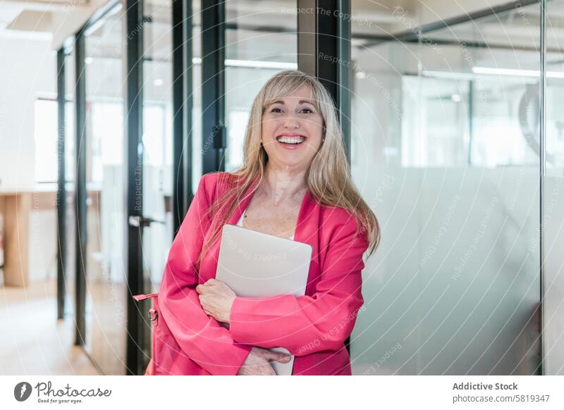 Selbstbewusste Geschäftsfrau mit Laptop in einem modernen Coworking Space Frau professionell Lächeln Selbstvertrauen Erfolg Büro stylisch Glas Wand rosa Blazer
