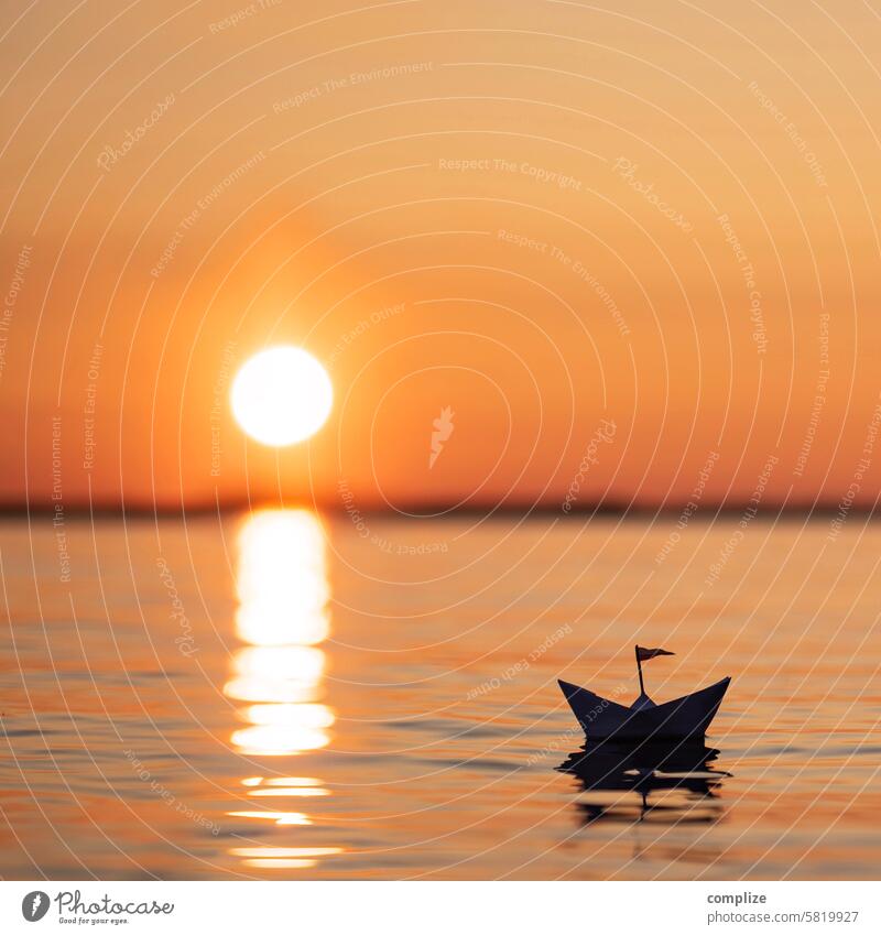 kleines Papierschiff fäht auf einem See in Finnland in den Sonnenuntergang sonne see meer wasser wellness relaxen ruhe abendrot boot orange schwimmen