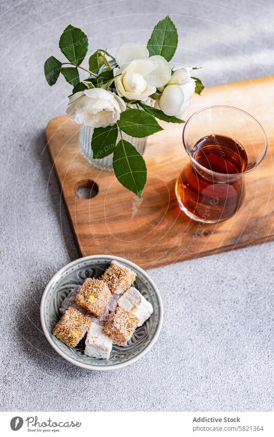 Türkische Köstlichkeiten und Tee mit weißen Rosen Dekor Freuden Schwarzer Tee Glas Vase weiße Rosen hölzern Holzplatte Teller sortiert mischen Snack süß