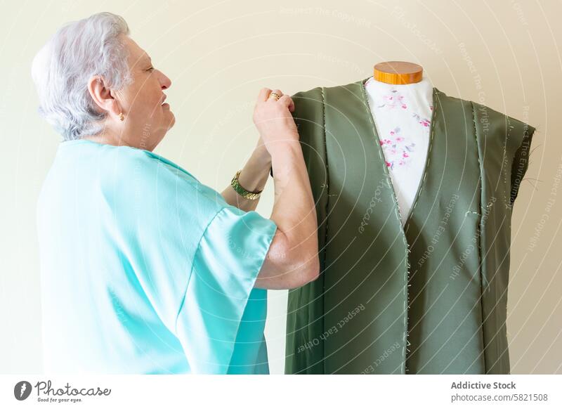 Ältere Näherin bei der Arbeit an einem Kleidungsstück auf einer Schaufensterpuppe älter Frau Schneidern Werkstatt Nähen Gewebe Handwerkskunst Designer Mode
