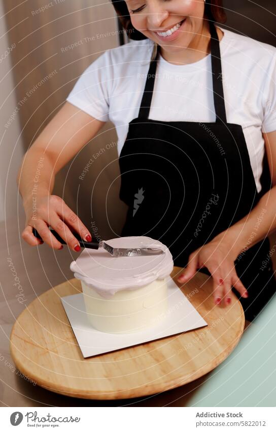 Frau glasiert einen Kuchen mit Präzision und Freude Zuckerguss backen Küche dekorierend Spachtel Lächeln Konditorei Gebäck Dessert Zuckerguß Koch Schürze