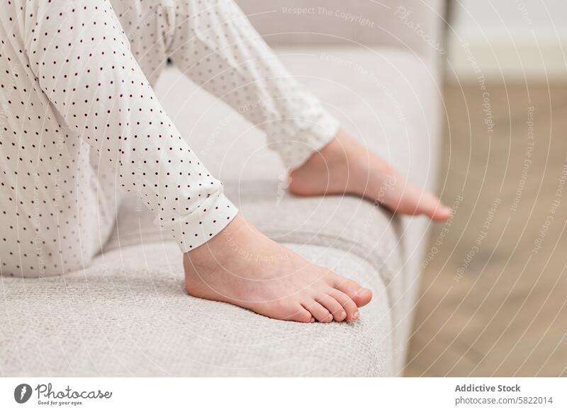 Nahaufnahme der nackten Füße eines Kindes im Schlafanzug zu Hause Fuß Barfuß Pyjama heimwärts Sofa Gewebe Textur Sitzen Komfort gemütlich sich[Akk] entspannen