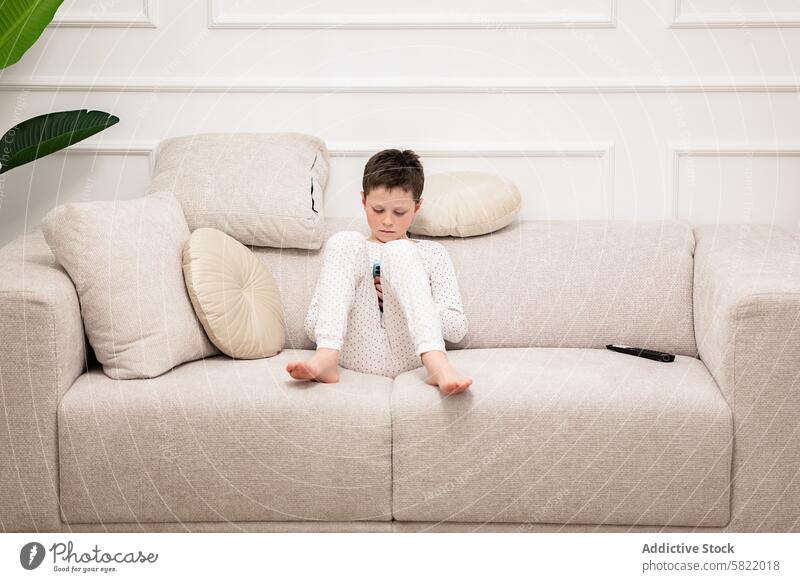 Kleiner Junge, der zu Hause in die Lektüre vertieft ist Kind lesen Buch heimwärts Liege Sitzen Pyjama fokussiert Windstille im Innenbereich Freizeit Aktivität