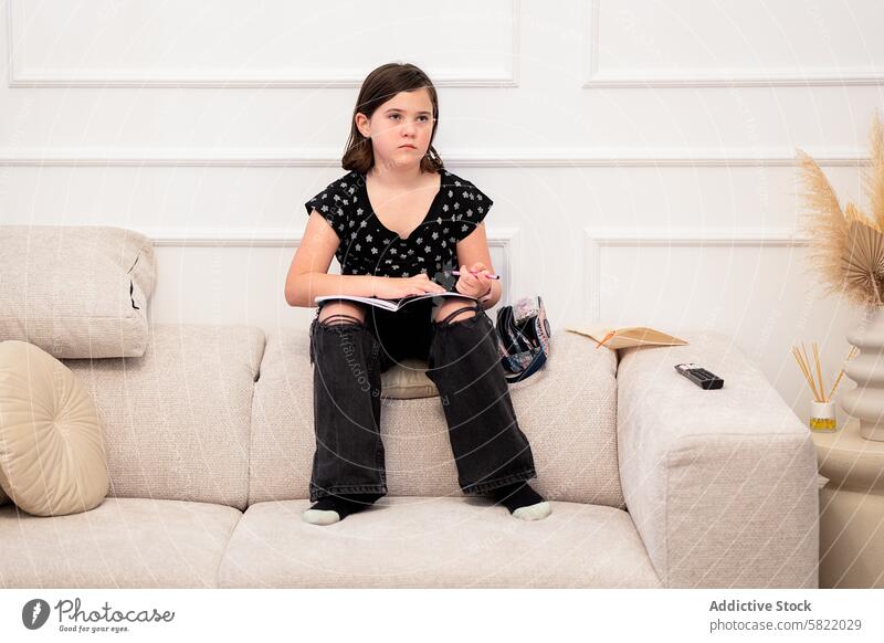Junges Mädchen liest auf dem Sofa mit nachdenklichem Gesichtsausdruck lesen heimwärts Buch besinnlich lässig wegschauen Kind Wohnzimmer bequem im Innenbereich