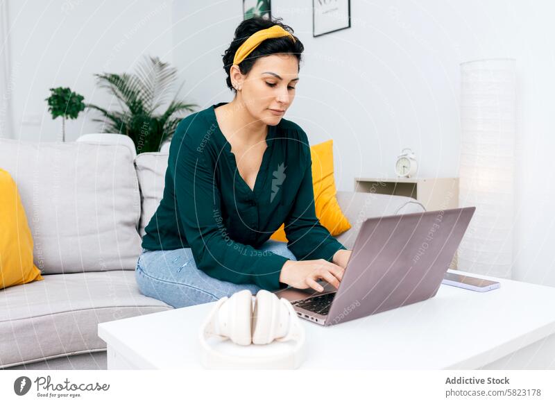 Frau, die in ihrem modernen Wohnzimmer am Laptop arbeitet arbeiten heimwärts Sofa bequem fokussiert im Innenbereich Minimalismus Dekor Technik & Technologie