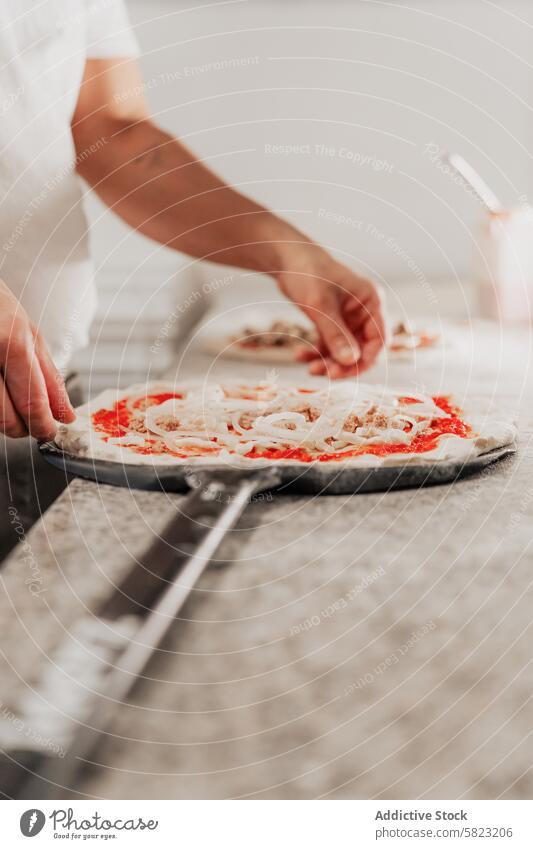 Klassische Pizza in einer professionellen Küche zubereiten Pizzeria Küchenchef Vorbereitung Essen zubereiten Belag Tomatensauce Zwiebel sich[Akk] schälen