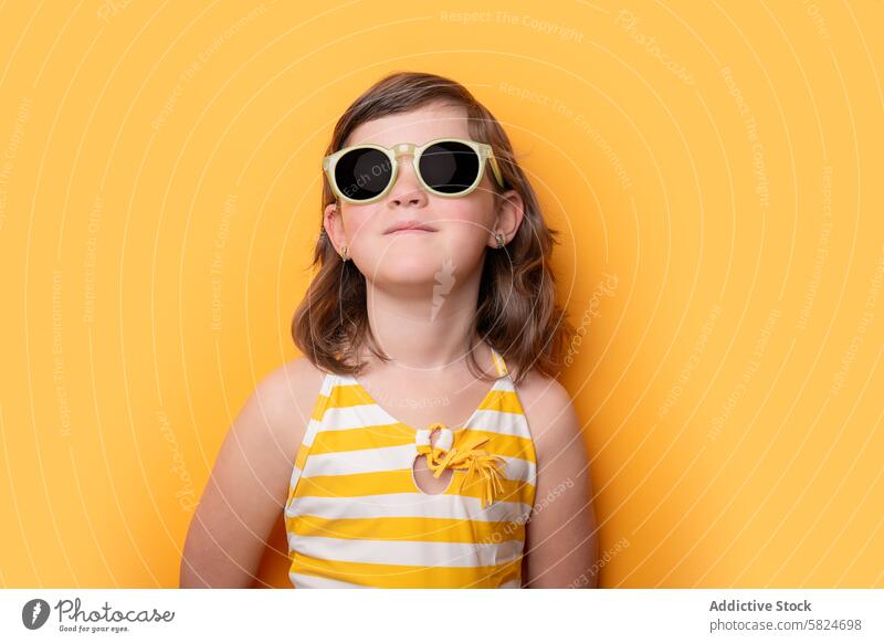 Junges Mädchen mit Sonnenbrille und gestreifter Badehose vor gelbem Hintergrund Lächeln gestreifte Badehose pulsierend Mode Kind Sommer Stil trendy jung Frau