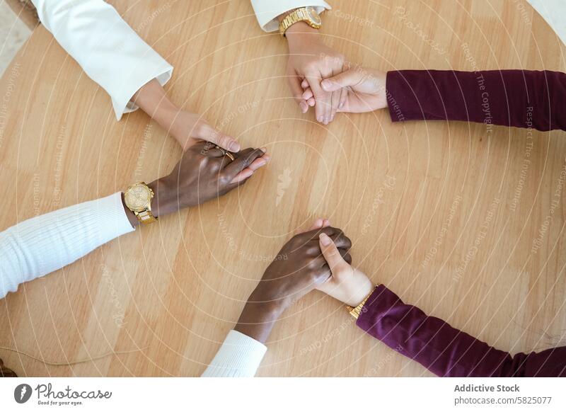 Verschiedene Frauen halten sich bei der Arbeit an den Händen, als Symbol der Zusammenarbeit Hand Vielfalt Einheit Teamwork Tisch modern Büro Kollege