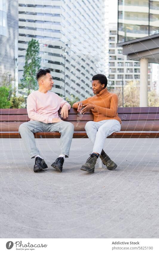 Zwei junge Freunde unterhalten sich auf einer städtischen Bank Gespräch plaudernd urban im Freien asiatischer Mann Afroamerikaner freundlich Dialog Sitzen