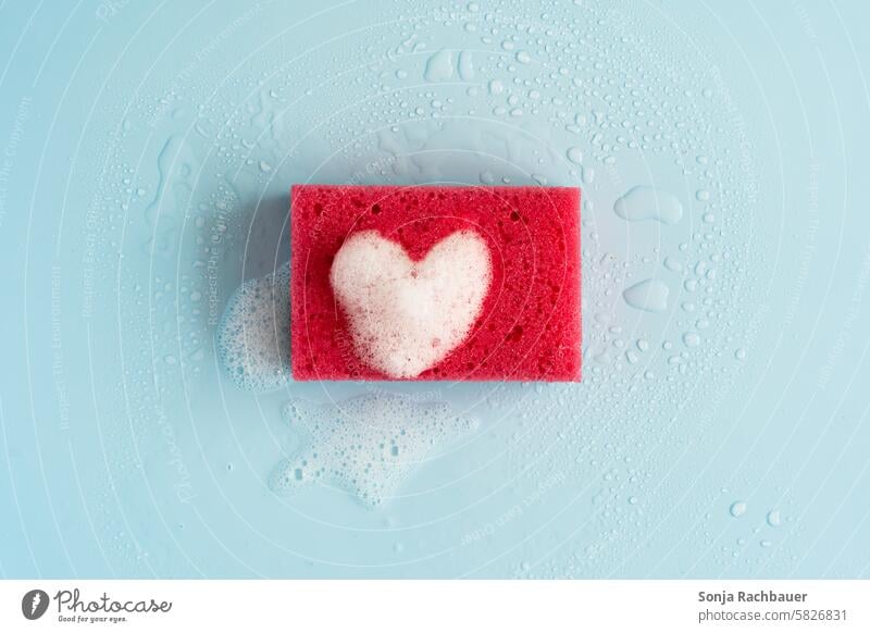 Ein roter Putzschwamm mit einem Herz aus Schaum. Draufsicht. Sauberkeit Reinigen Wasser nass Blauer Hintergrund putzen Reinlichkeit Häusliches Leben