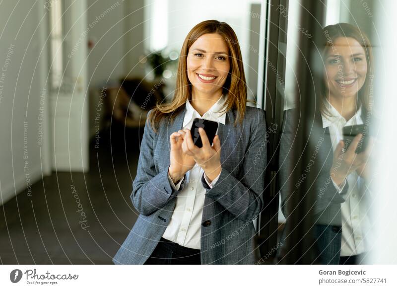 Lächelnde Geschäftsfrau in modernem Büro mit Smartphone in der Hand genießt einen erfolgreichen Arbeitstag professionell Gang Reflexion & Spiegelung Business