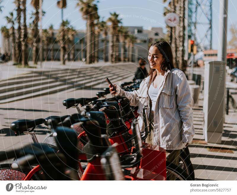 Ein heiterer Frühlingsnachmittag in Barcelona mit einer lächelnden Frau, die ein Fahrrad mietet Abtastung Öffentlich Telefon ökologisch Zyklus Radfahren