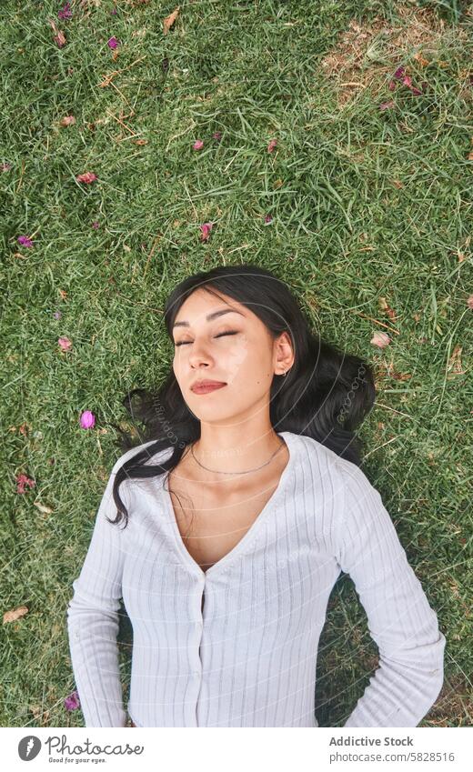 Gelassene Frau, die einen entspannenden Moment in der Natur genießt Park Gelassenheit Ruhe Gras Augen geschlossen Freizeit im Freien Erholung Grün jung ruhen