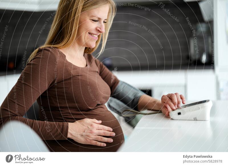 Schwangere Frau misst ihren Blutdruck zu Hause Schwangerschaft schwanger Erwachsener Vorfreude wartend Baby Bauch Geburt Körper Pflege Kaukasier Kind