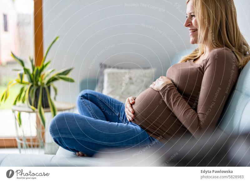 Schwangere Frau, die ihren Bauch berührt, entspannt auf dem Sofa zu Hause Schwangerschaft schwanger Erwachsener Vorfreude wartend Baby Geburt Körper Pflege