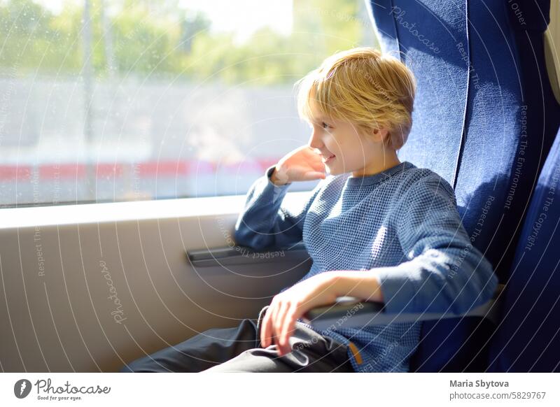 Niedlicher Junge im Teenageralter reist in einem Nahverkehrswagen oder mit der Eisenbahn, während es draußen regnet. Vorstadt Zug Mitfahrgelegenheit Kind lokal