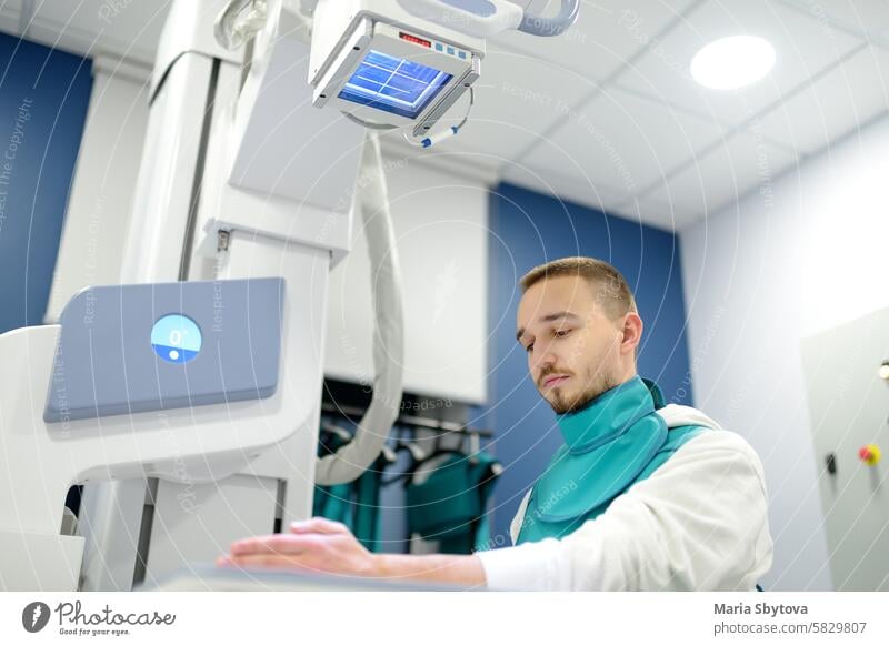 Junger Mann mit Röntgenaufnahme einer gebrochenen Hand im Röntgenraum einer modernen Klinik. Patient trägt zum Schutz eine Bleischürze Radiologin röntgen Schuss