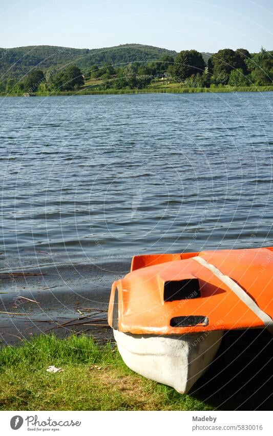 Altes Tretboot aus Kunststoff in leuchtendem Orange am Ufer im Sommer vor blauem Himmel im Sonnenschein am Poyrazlar Gölü bei Adapazari in der Provinz Sakarya in der Türkei