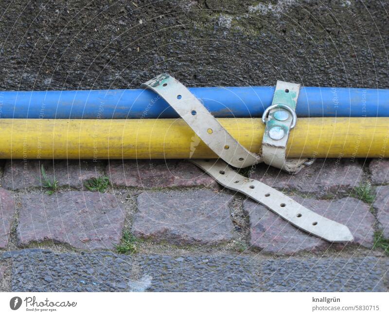 Lockere Bindung Kabel Befestigung Zusammenhalt Gürtel weiß blau gelb grau nebeneinander Nahaufnahme Farbfoto liegen Pflastersteine Rinnstein Außenaufnahme Tag