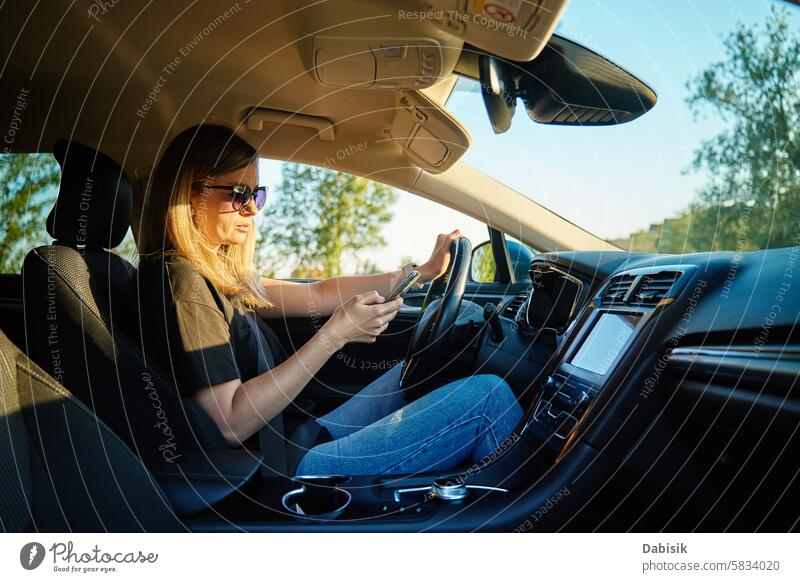 Frau benutzt Smartphone während der Fahrt im Auto PKW fahren Sonnenbrille Fahrer Sicherheit Ablenkung Straße Fahrzeug Nachmittag sonnig Sitz Gerät